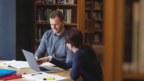 Two students studying in front of bookcase