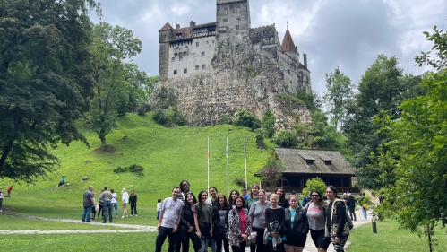 Group of people standing in front of green field and a large stone castle