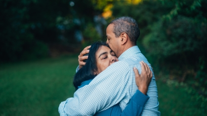 Two adults hugging; one female presenting and one male presenting; comforting embrace