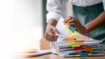 Photo of a stack of printed papers with colorful post-it notes attached and separated by binder clips