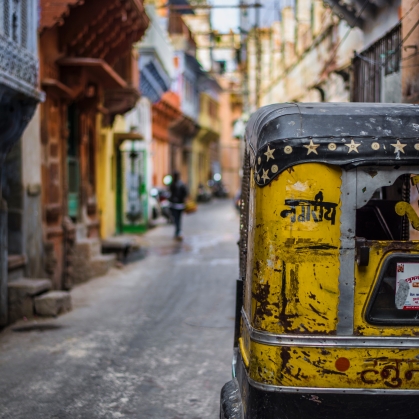 Colorful street with rows of homes on either side with the back of a yellow taxi-cart in the right corner