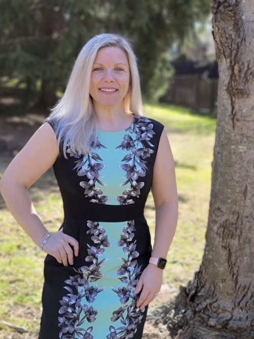 Melissa Shermer outside in front of tree in blue and black dress