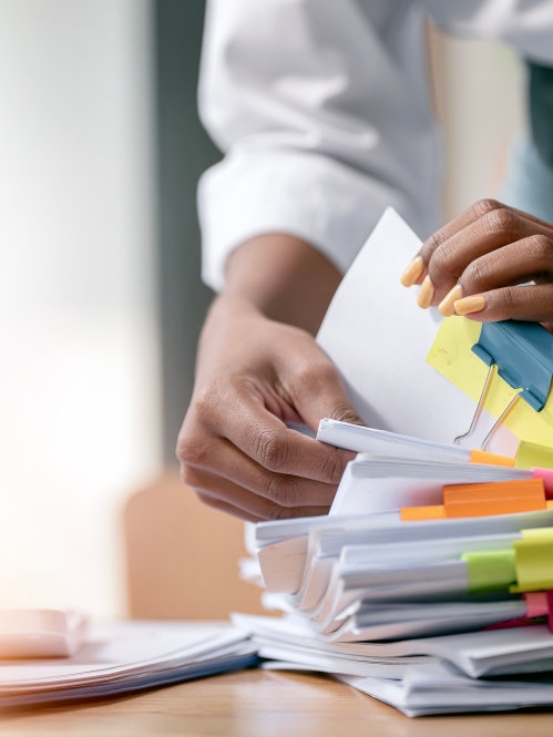 Photo of a stack of printed papers with colorful post-it notes attached and separated by binder clips