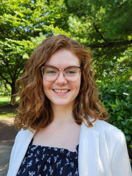 Photo of woman with red hair and glasses in front of trees