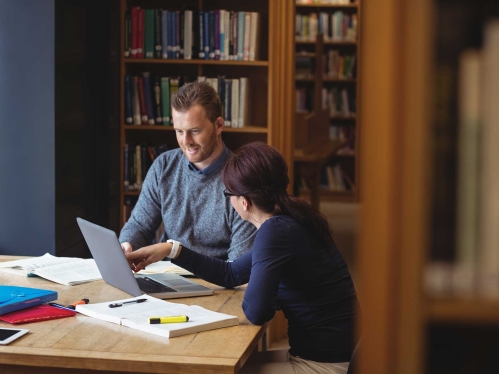 Two students studying in front of bookcase