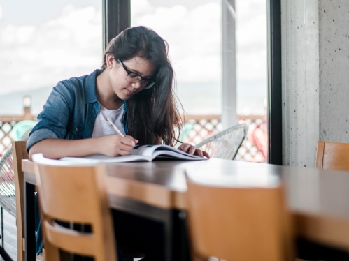 Young woman with glasses and brown hair reading at a long wooden table