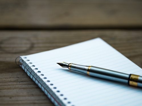 image of an open notebook on a wood desk with an ink pen laying on top