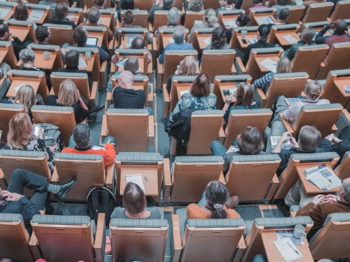 Overhead photo of a large room with many seats. The photo is of the tops of people's heads sitting in the seating