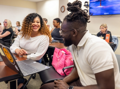 Classroom with adult learnings; camera focus is on two students engaged with each other and smiling